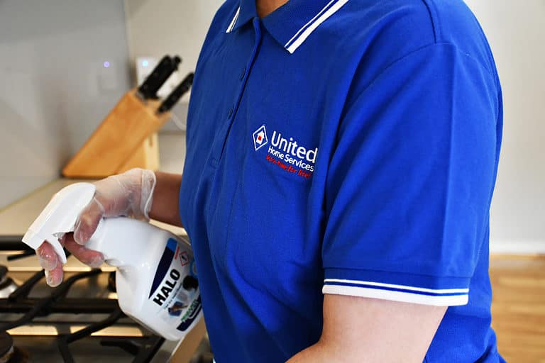 Cleaner in UHS shirt using kitchen spray on stove top